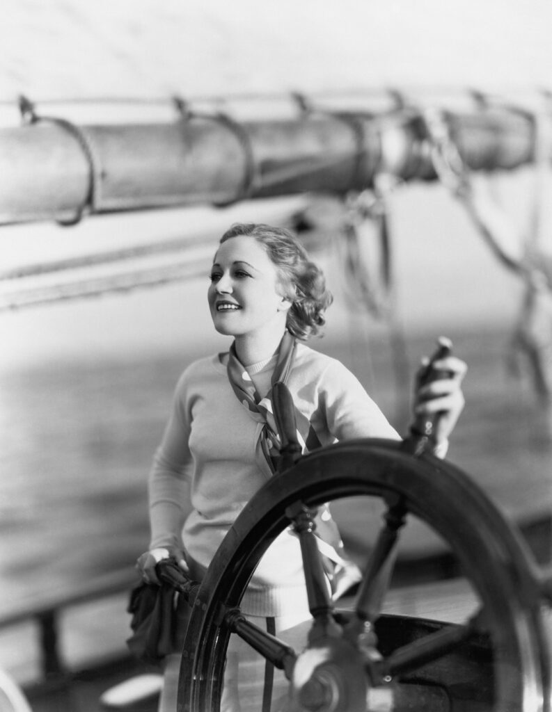 An elegant young women, with the breeze in her hair, stands at the helm of a sailing ship. Looking happy and to a bright future of sustainable investing!
